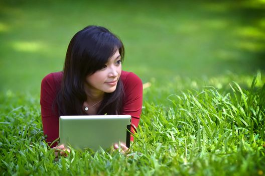 pretty woman using tablet outdoor laying on grass