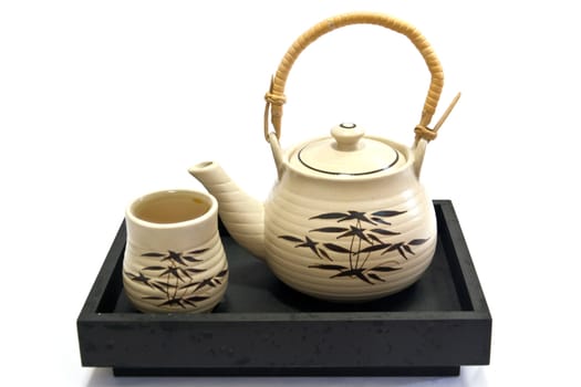 Teapot and teacup painting bamboo leaves on a black tray.