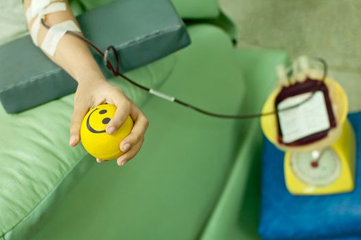 a donor in an armchair donates blood at hemotransfusion station with smiley ball in hand
