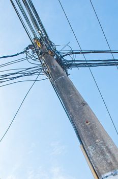 Energy and technology: electrical post by the road with power line cables, transformers and phone lines against bright blue sky providing copy space.