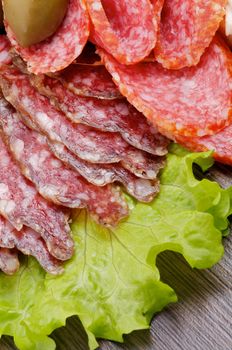 Slices of Salami and Smoked Sausage on Lettuce with Green Olive closeup