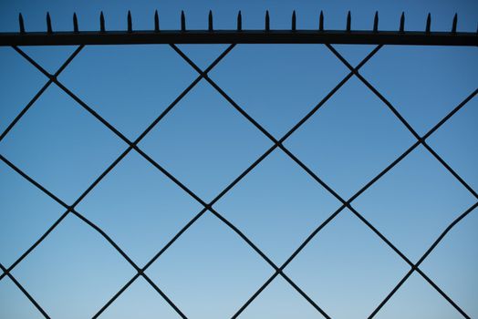 Metal fence with sharp spikes at the top against great blue sky