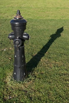 Old black fire hydrant in a meadow with great shadows