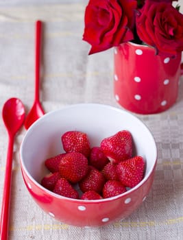 Red bowl with strawberries for breakfast next is a cup with red roses