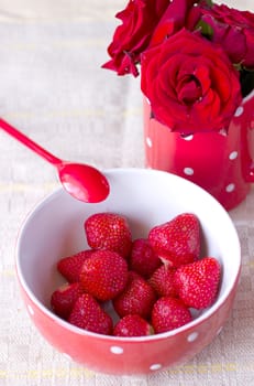 Red bowl with strawberries for breakfast next is a cup with red roses