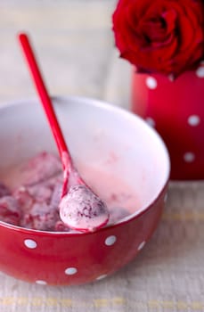 Red bowl with strawberries and cream for breakfast is next cup with red roses