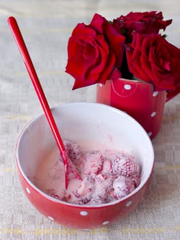 Red bowl with strawberries and cream for breakfast is next cup with red roses