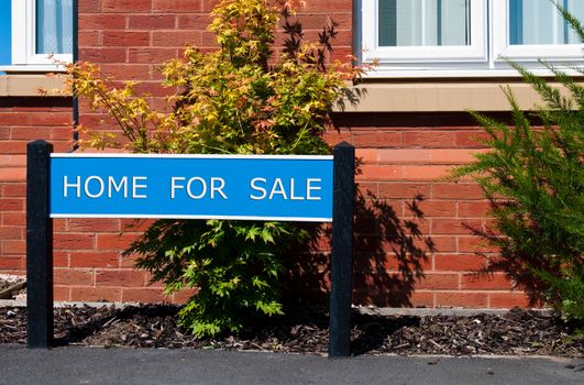 home for sale real estate sign in front of new house with garden