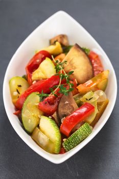 Bowl of fresh homemade Ratatouille made of eggplant, zucchini, bell pepper and tomato and seasoned with herbs (garlic, thyme, oregano) (Selective Focus, Focus on the front leaves of the thyme sprig on the meal)