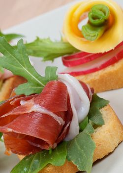 Jamon and Cheese Appetizers with Greens, Onion and Radish close up on gray plate