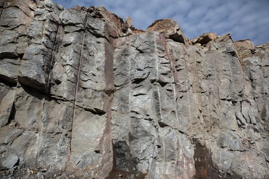 The cut man-made rock with explosive technology close up against the sky with clouds