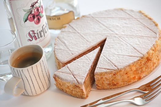 Photo of a Zuger Kirschtorte, with bottles of kirsch schnapps and coffee. Labels on bottles are not real product labels and created for this photo.

