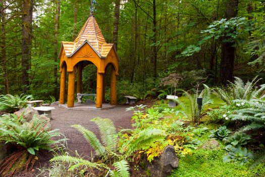 A bautiful natural outdoor garden has a path, greens, ferns, a patio area, and a wooden gazebo. This is a wedding location in the Pacific Northwest, Oregon.