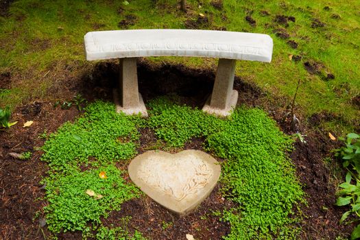 A beautiful stone bench sits next to some green clover and a heart shaped stone tile piece in a perfectly manicured garden in Oregon.