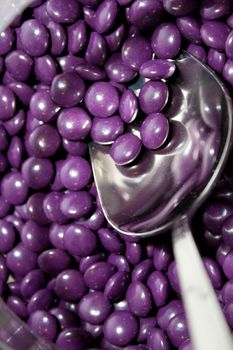 A silver spoon rests in a dish with purple candy at a wedding candy bar for the guests.