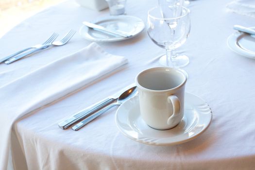 A white serving set includes silverware, a mug, a saucer, and a wine glass at the reception for a wedding.