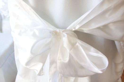 At a wedding a white bow and linens cover a chair for the guests.