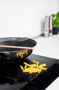 Frying pan, sticks and pasta in modern kitchen with induction stove