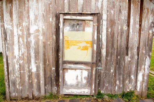 An old building with a peeling paint wood texture and a very old door on a shed or barn creates an abstract background image.