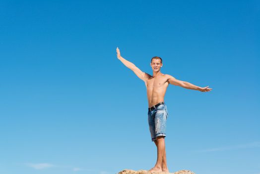 shirtless man spread his hands against the blue sky