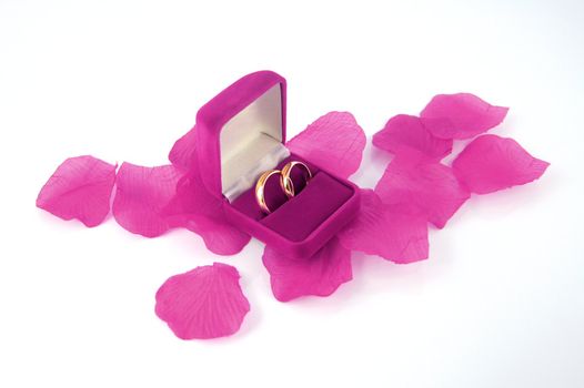 Wedding rings inside a pink box located on material rose petals