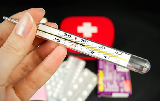 Hand holding thermometer, some of medicines in background