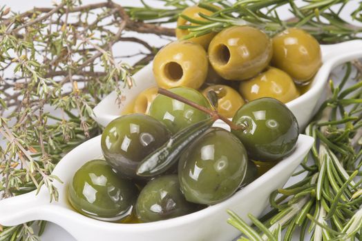 Two china spoons with green and pitted olives and some aromatic herbs
