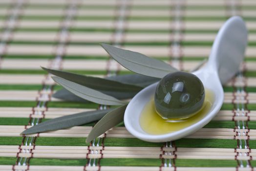 China spoon with olives a its leaves on a bamboo mat