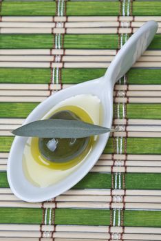 China spoon with olives a its leaves on a bamboo mat