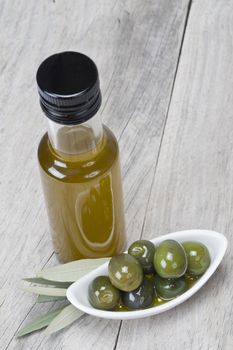 Olive oil bottle and some olives in a china spoon on a wooden surface