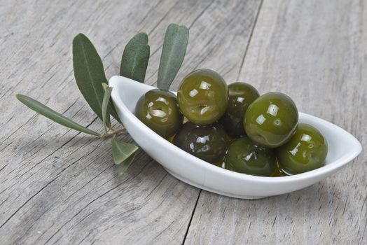 A china spoon with olives and leaves on a wooden surface
