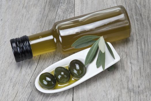 Olive oil bottle and some olives in a china spoon on a wooden surface