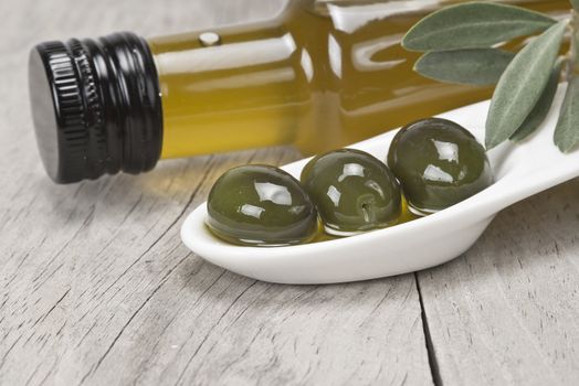 Olive oil bottle and some olives in a china spoon on a wooden surface