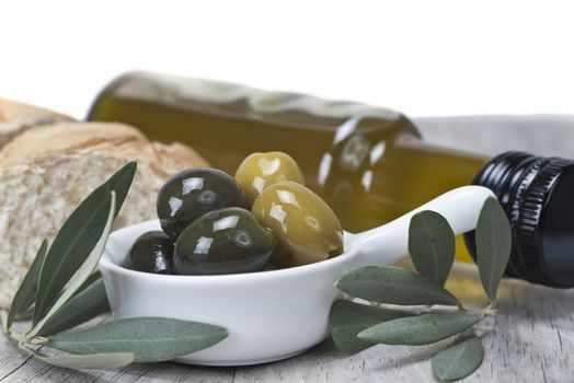 Olive oil with green olives and bread on a wooden surface