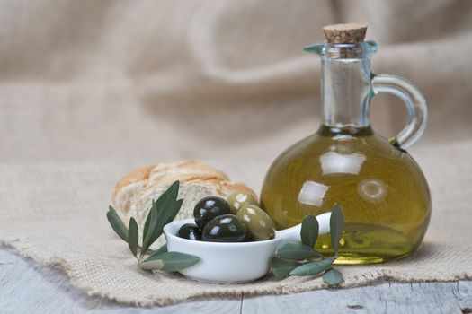Olive oil with green olives and bread on a wooden surface