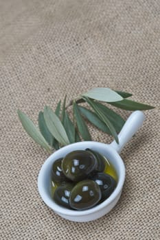 A china spoon with olives and leaves on a burlap surface