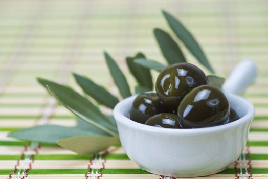 China spoon with olives a its leaves on a bamboo mat