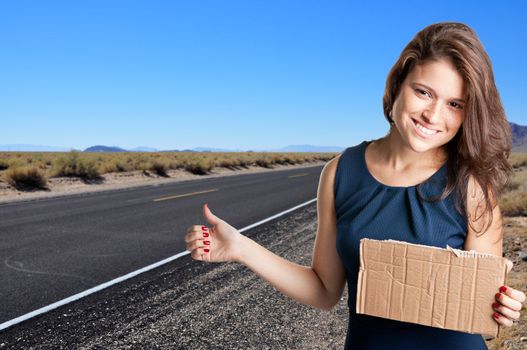Young woman hitch hiking at a desert road holding a cardboard