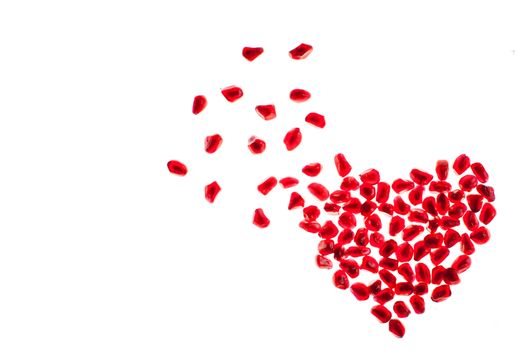 blowing heart shape made by pomegranate seeds isolated on white