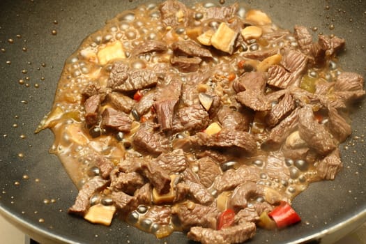 beef meat stewing with red peppers in black frying pan