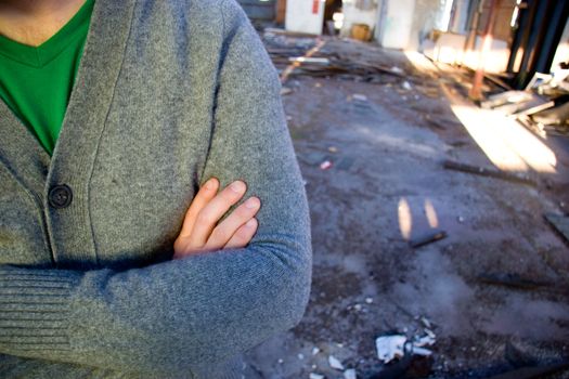 A man wearing a sweater folds his arms at a dirty warehouse building.