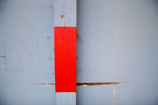 A square of red paint on a grey blue wall with writing and cracks.