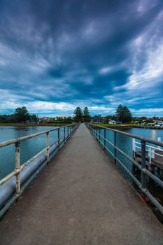 Evening footbridge walkway across Moyne River in Port Fairy, VIC. Calm water with dramatic cloud overhead.