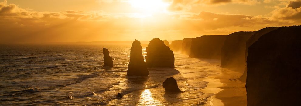 Golden sunset at 12 Apostles rock formation in Victoria, Australia. Dusk sun setting behind the backlit apostles with sea fog rolling in to the cliff face.