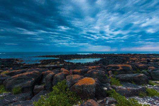 Dusk (Sunset) over black volcanic rocky tidal pool and sky full of rolling cloud in Port Fairy, Victoria, Australia.