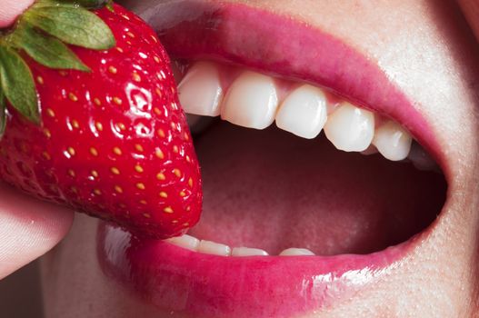 Macro close up of a beautiful female mouth eating a fresh strawberry