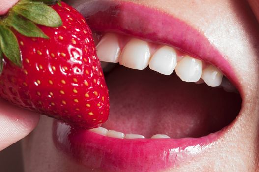 Macro close up of a beautiful female mouth eating a fresh strawberry
