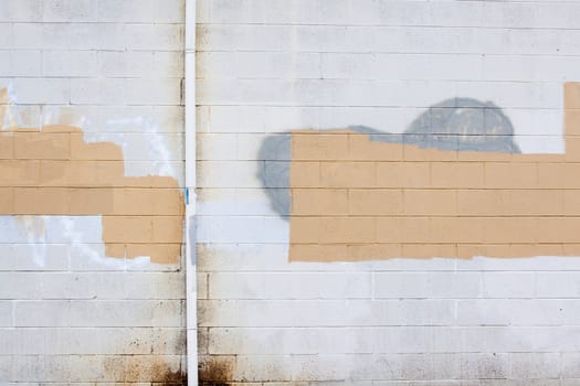 A grey wall has rectangular and square patches of paint used to cover up graffiti and vandalism along the side of an urban building.