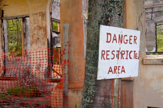 A hand written sign by an old home that is falling apart and crumbling to the ground.