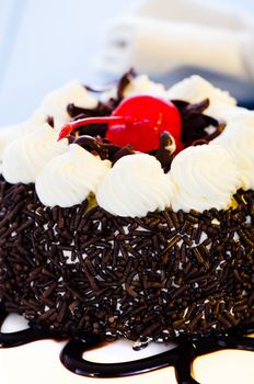 Small chocolate cake with white cream and cherry as decoration